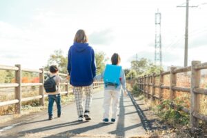 小学生と幼児の子どもを連れて歩く母親。母子家庭の母と子が下校の帰り道を歩く後ろ姿。