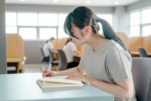 大学の自習スペースでノートを取りながら勉強する学生。母子家庭でも進学を諦めず、奨学金や支援制度を活用して未来へ進む姿をイメージした写真。