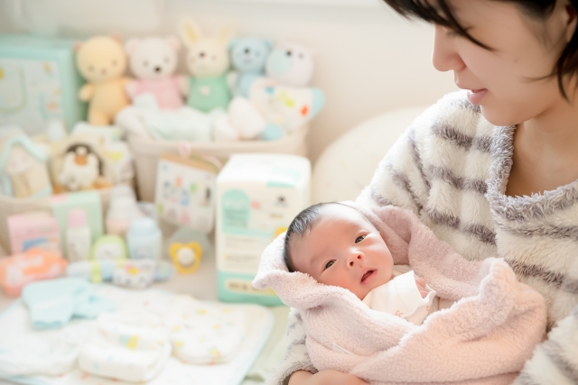 赤ちゃんを抱く母子家庭のお母さん。生活保護の支援で赤ちゃん用品が整い、安心して子育てをする様子。