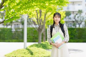 母子家庭で育った娘が専門学校のキャンパスで笑顔を見せる姿。奨学金や給付金制度を活用して夢に向かって進学を叶えたイメージ。