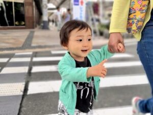 母子家庭の親子が手をつないで横断歩道を渡る様子。子どもが笑顔で指をさし、安心して歩ける街の雰囲気が伝わる。