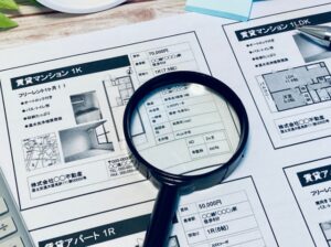 母子家庭がマンションの賃貸情報を比較しながら家賃や条件を確認している様子を表す不動産資料とルーペの写真